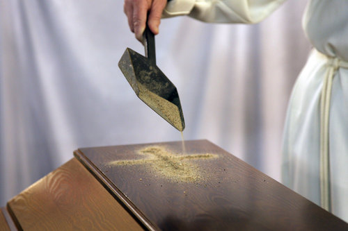 Pappi tekee hiekasta ristinmerkin arkun päälle. Kirkon kuvapankki/Aarne Ormio.