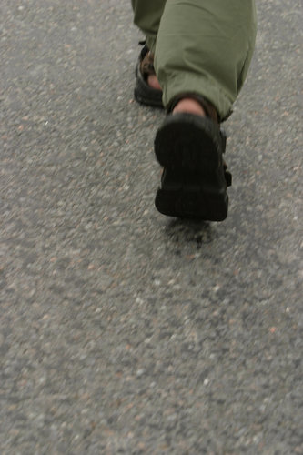 Kävelijä sandaalit jalassa märällä asfaltilla.
