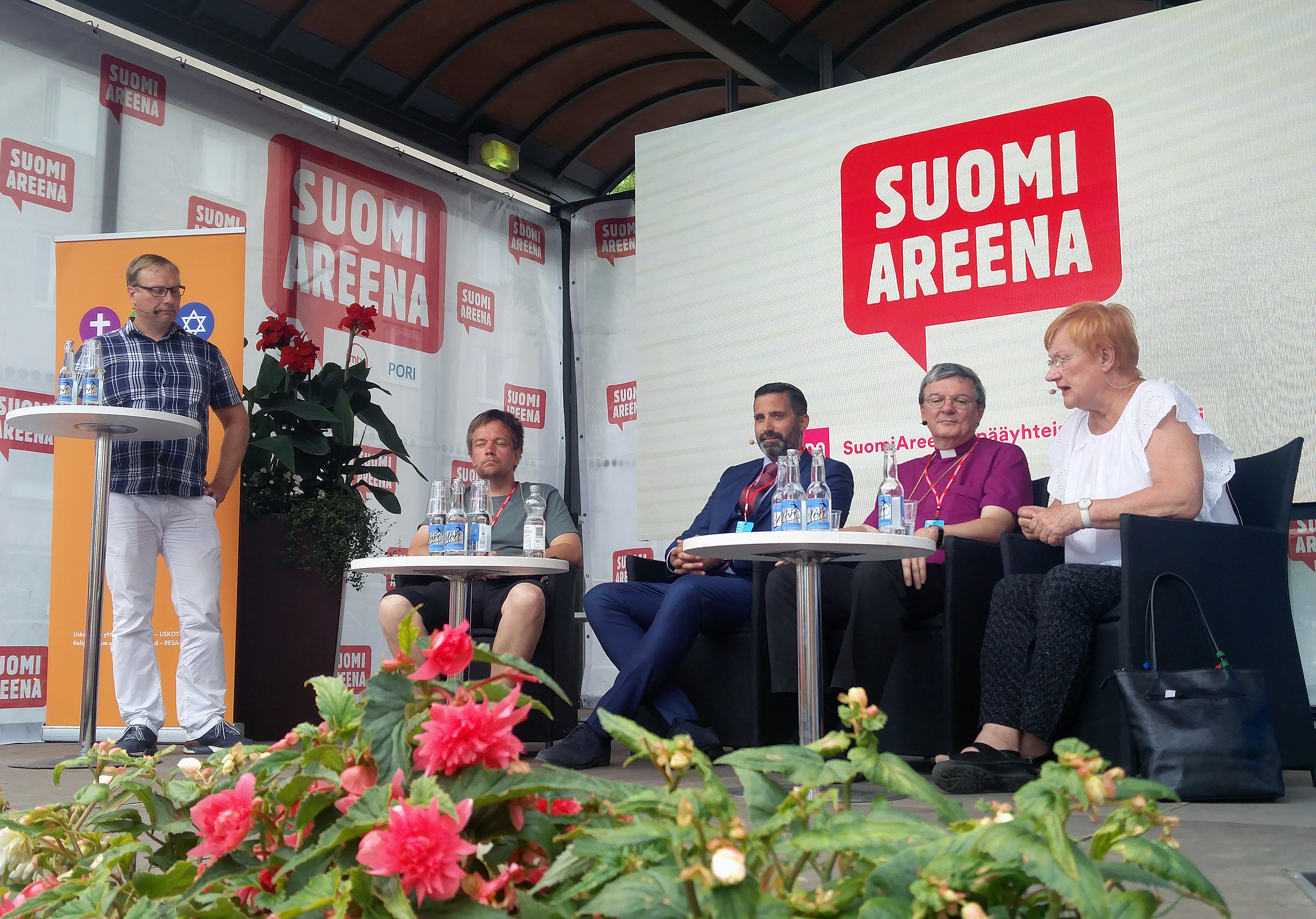 Neljä panelistia istuu ja yksi seisoo lavalla keskustelemassa.